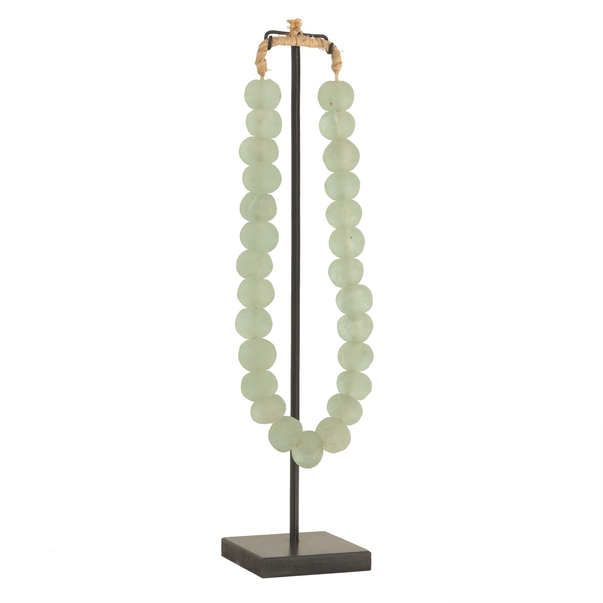 Decorative strand of recycled glass beads in a soft green hue, displayed on a minimalist black metal stand. A unique accent piece that adds texture and artisanal charm to any interior styling