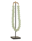 Decorative strand of recycled glass beads in a soft green hue, displayed on a minimalist black metal stand. A unique accent piece that adds texture and artisanal charm to any interior styling