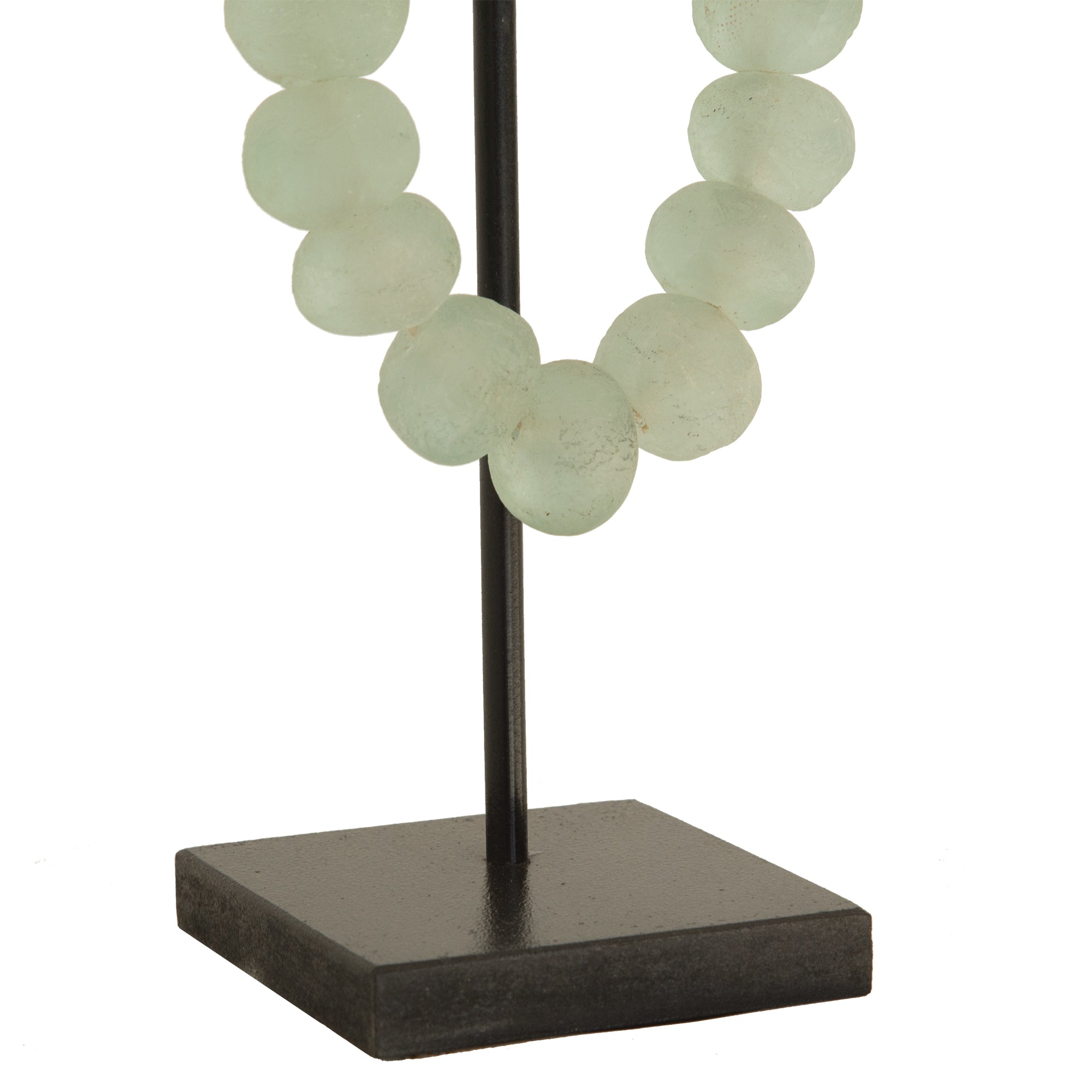 Decorative strand of recycled glass beads in a soft green hue, displayed on a minimalist black metal stand. A unique accent piece that adds texture and artisanal charm to any interior styling