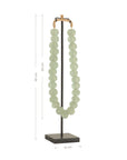 Decorative strand of recycled glass beads in a soft green hue, displayed on a minimalist black metal stand. A unique accent piece that adds texture and artisanal charm to any interior styling