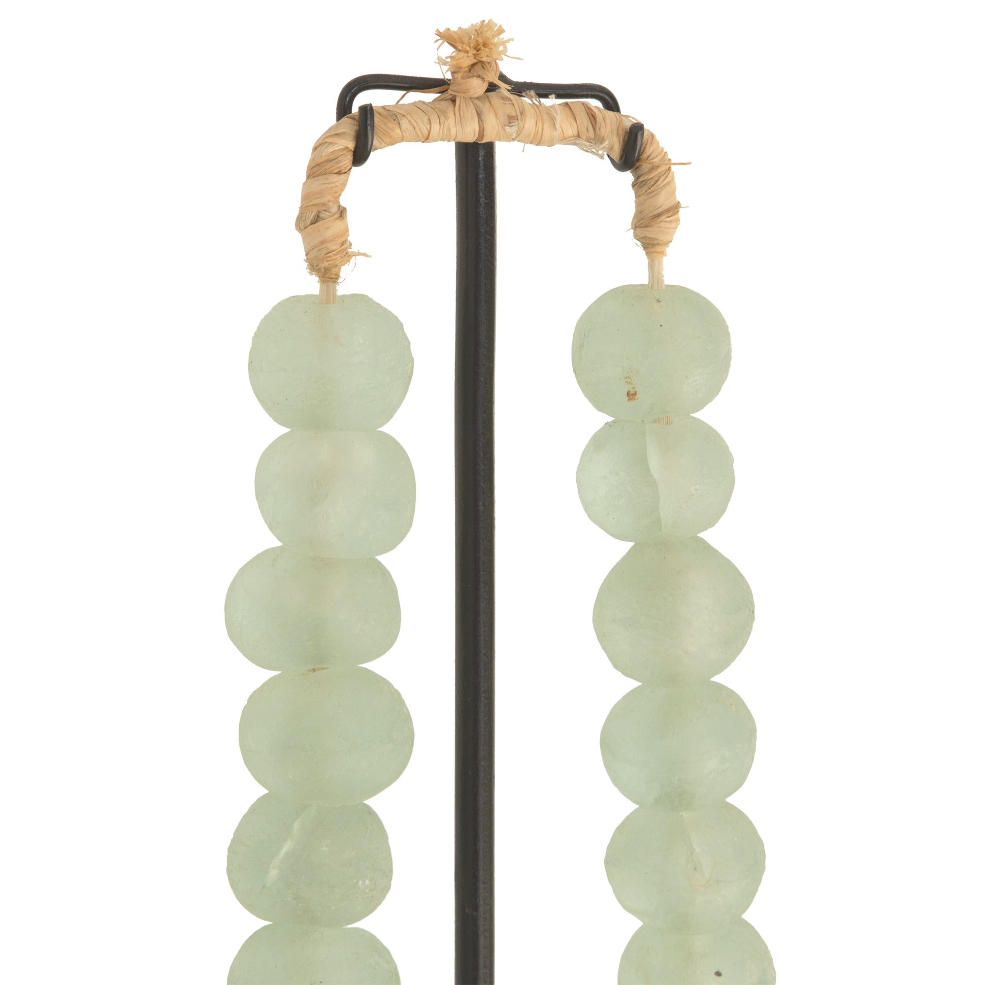 Decorative strand of recycled glass beads in a soft green hue, displayed on a minimalist black metal stand. A unique accent piece that adds texture and artisanal charm to any interior styling