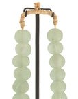 Decorative strand of recycled glass beads in a soft green hue, displayed on a minimalist black metal stand. A unique accent piece that adds texture and artisanal charm to any interior styling