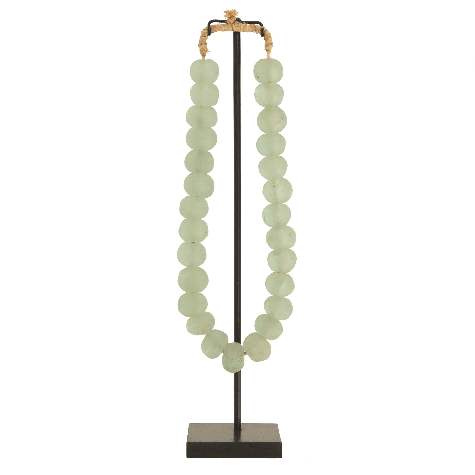 Decorative strand of recycled glass beads in a soft green hue, displayed on a minimalist black metal stand. A unique accent piece that adds texture and artisanal charm to any interior styling