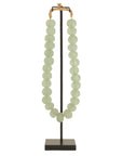 Decorative strand of recycled glass beads in a soft green hue, displayed on a minimalist black metal stand. A unique accent piece that adds texture and artisanal charm to any interior styling