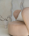 Modern lounge corner featuring a beige teddy armchair with a linen cushion, styled beside a sculptural wavy mirror. Neutral-toned ceramics and organic branches complete the serene, minimalist aesthetic