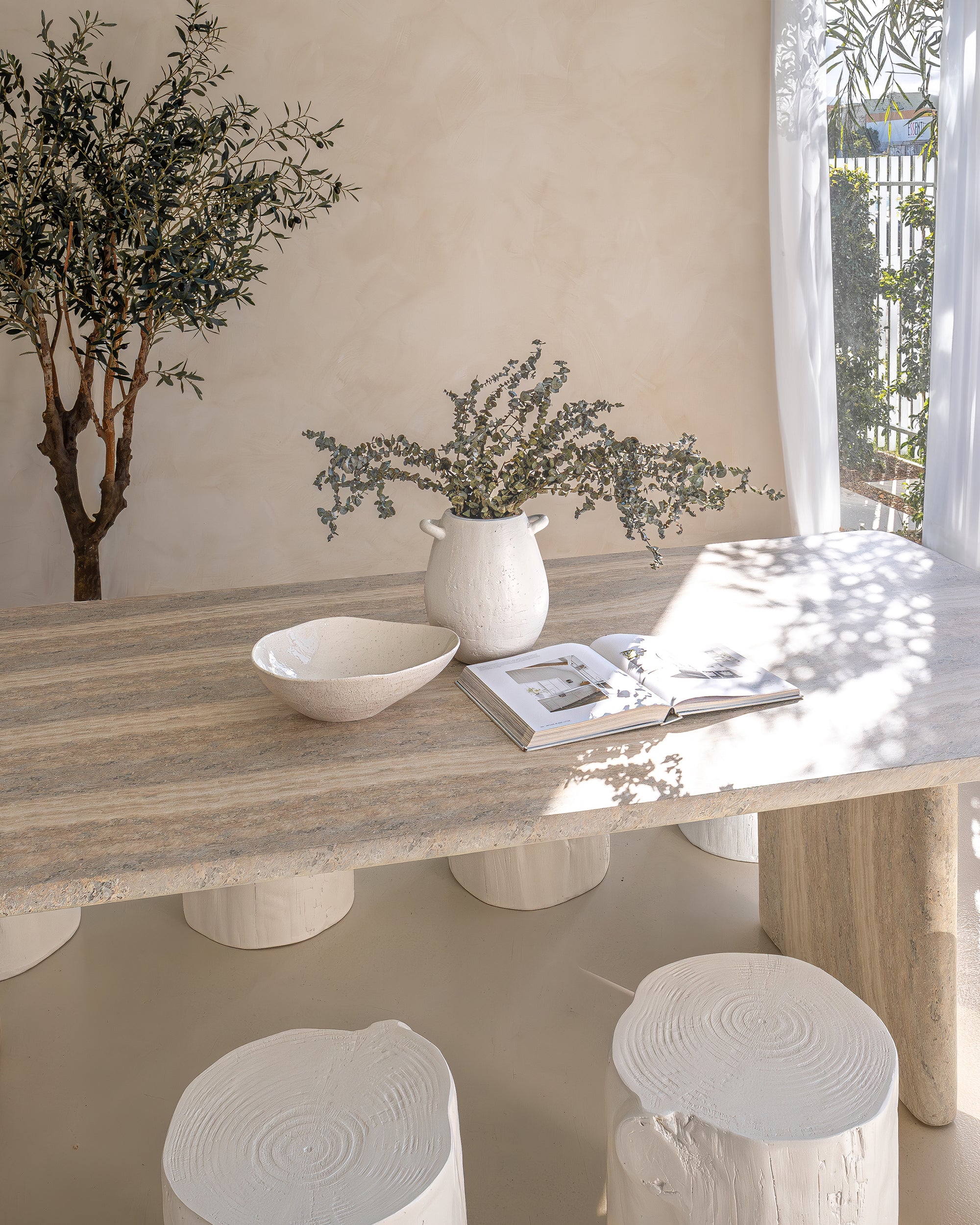 Hydro dipped dining table styled with white timber stump stools, neutral linen napkins, and ceramic tableware. A soft, sunlit setting with organic textures and natural elements, creating a relaxed, earthy ambiance