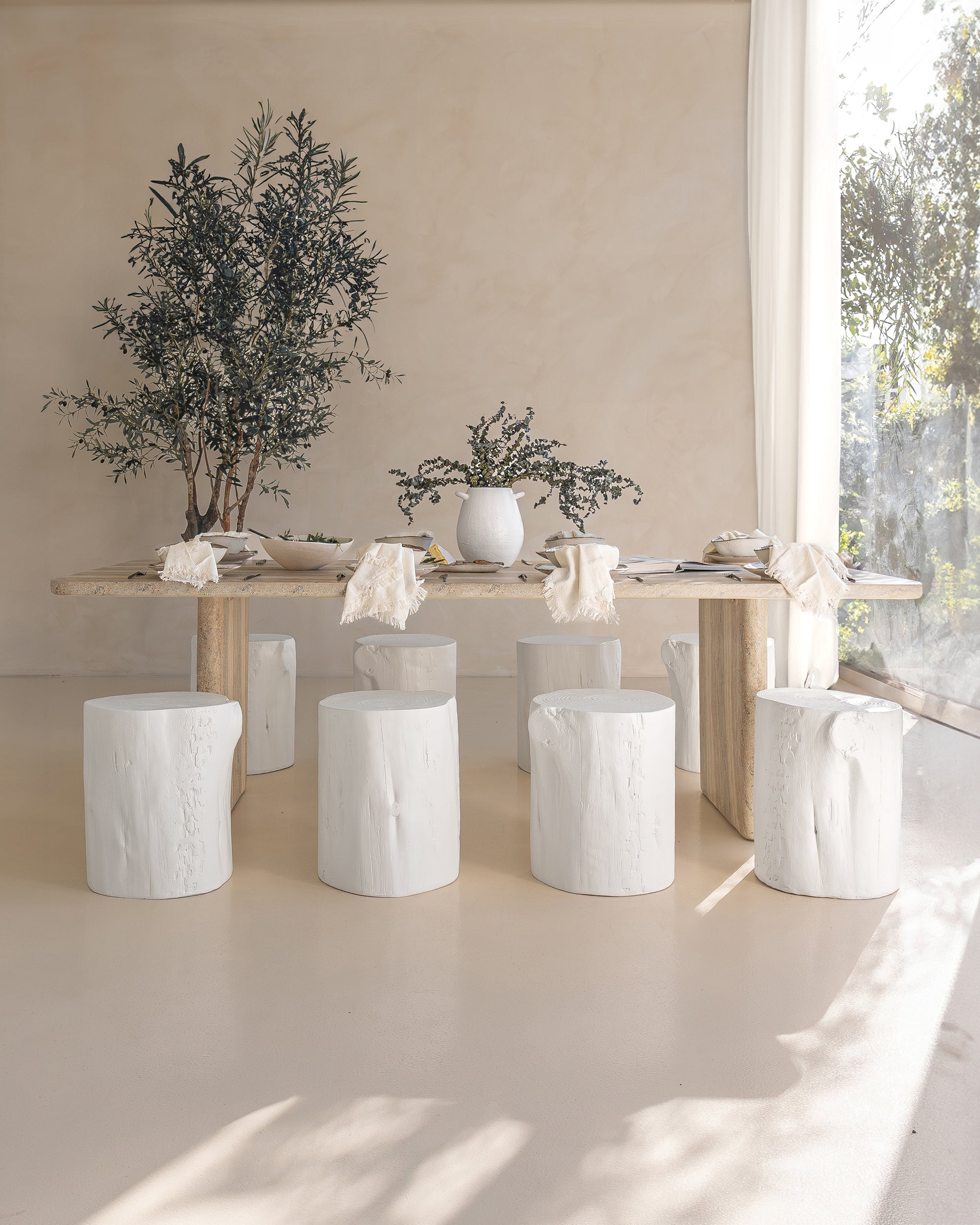 Hydro dipped dining table styled with white timber stump stools, neutral linen napkins, and ceramic tableware. A soft, sunlit setting with organic textures and natural elements, creating a relaxed, earthy ambiance