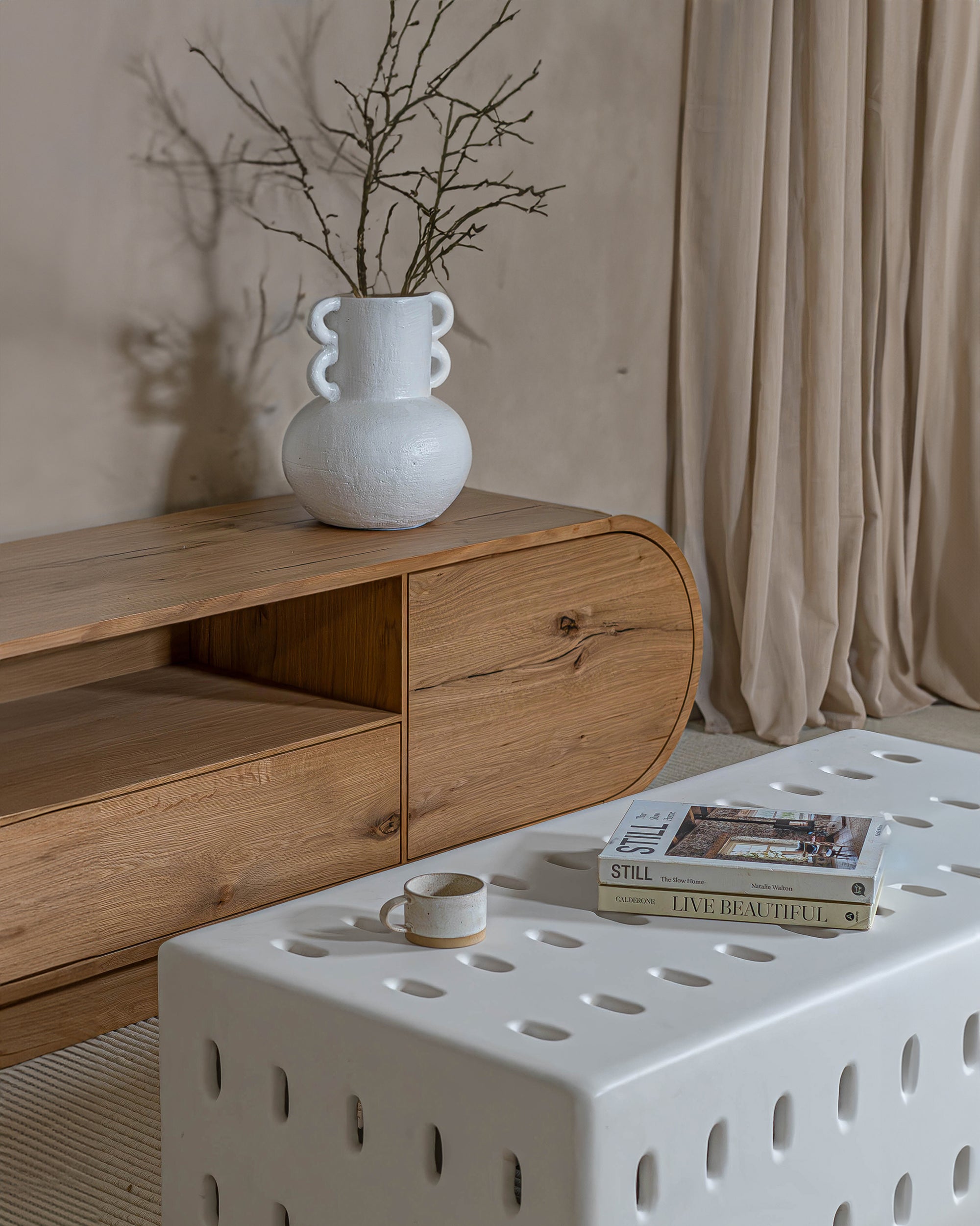 Modern living space featuring a natural oak TV unit paired with a sculptural white ceramic coffee table, styled with a statement vase, books, and a ceramic cup for a refined aesthetic.