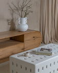 Modern living space featuring a natural oak TV unit paired with a sculptural white ceramic coffee table, styled with a statement vase, books, and a ceramic cup for a refined aesthetic.