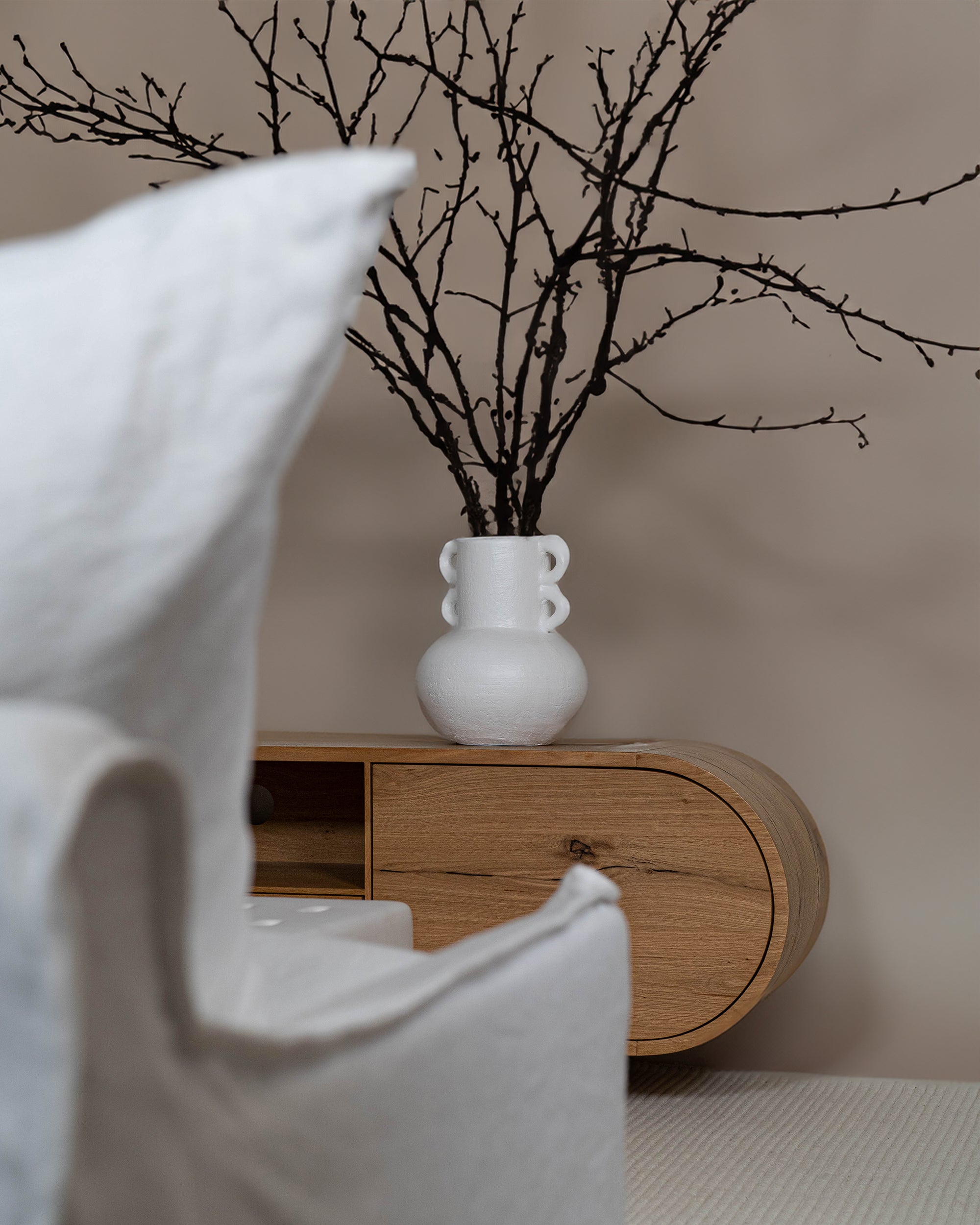 Modern living space featuring a natural oak TV unit paired with a sculptural white ceramic coffee table, styled with a statement vase, books, and a ceramic cup for a refined aesthetic