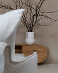 Modern living space featuring a natural oak TV unit paired with a sculptural white ceramic coffee table, styled with a statement vase, books, and a ceramic cup for a refined aesthetic