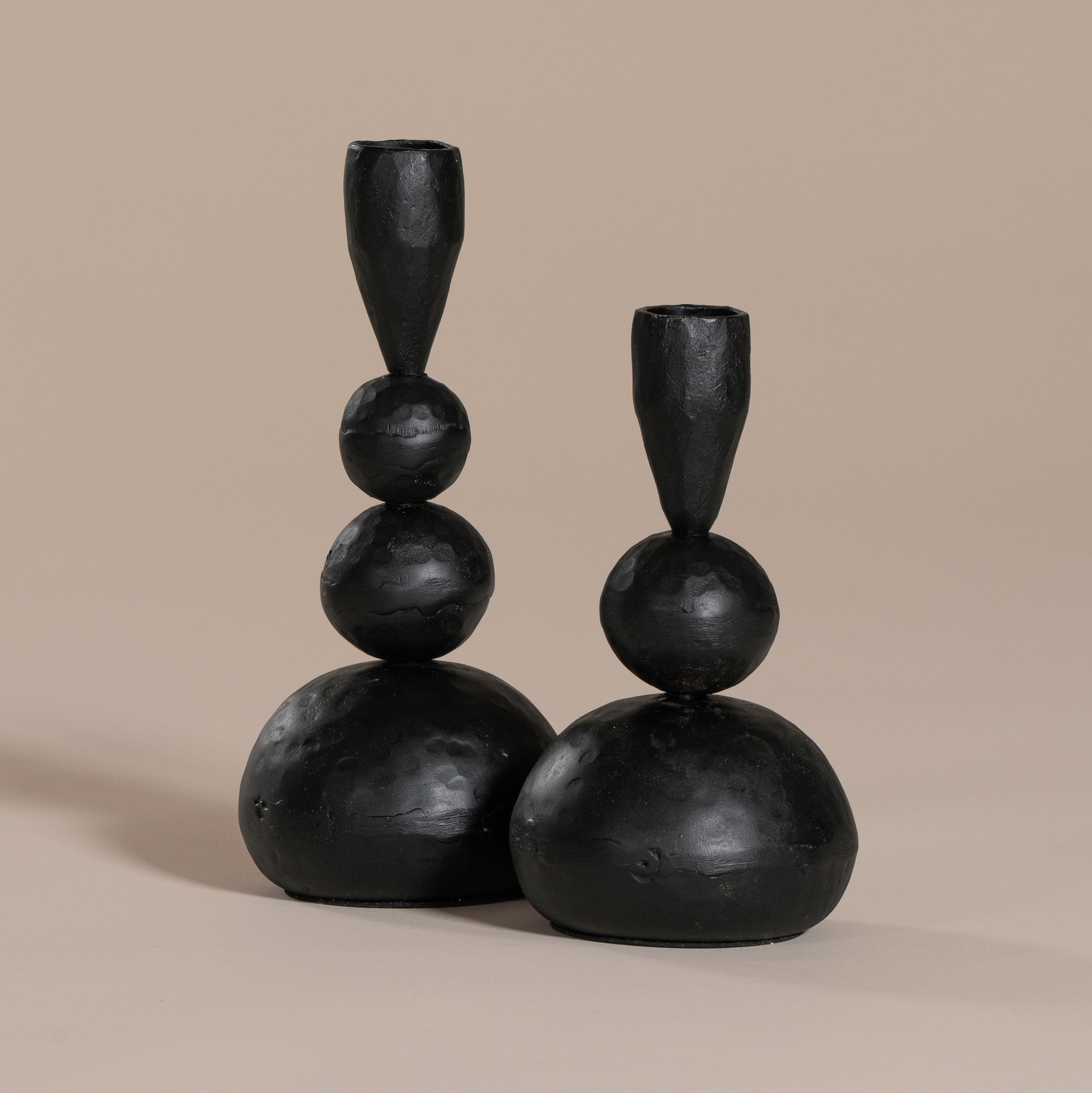 A pair of sculptural black iron candle holders with an organic, modern design, elegantly placed in a soft beige arched wall niche, creating a warm and minimalist aesthetic