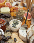 A beautifully styled grazing board featuring KULALA Living’s black cheese knife, artisanal cheeses, hummus topped with pumpkin seeds, dried fruits, crackers, and gourmet accompaniments. A sophisticated spread perfect for effortless entertaining