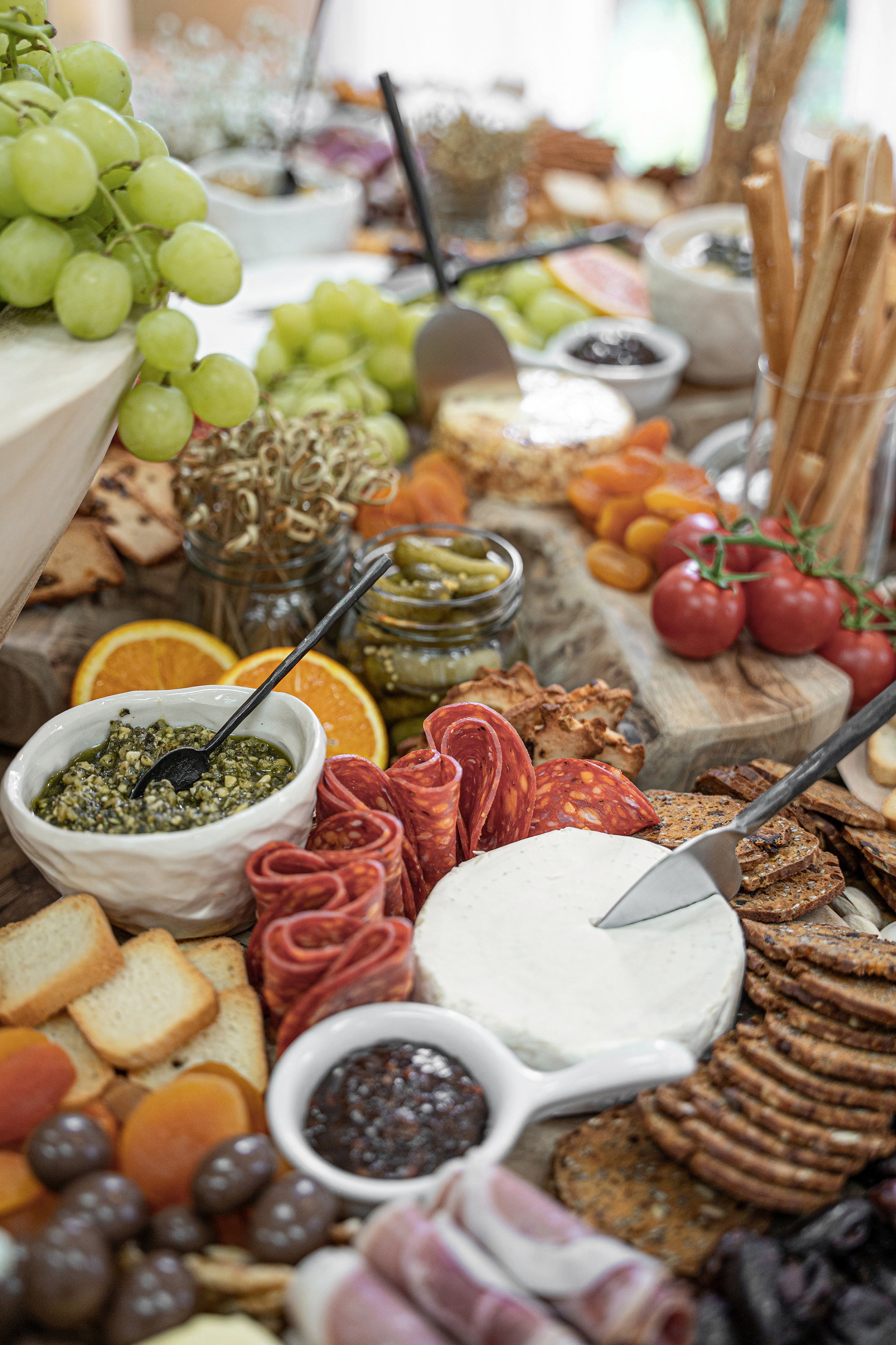 An abundant grazing board featuring KULALA Living’s black hand-forged cheese knife slicing through creamy brie. Surrounded by gourmet crackers, cured meats, fresh fruit, and savoury dips, this scene embodies effortless, elevated entertaining