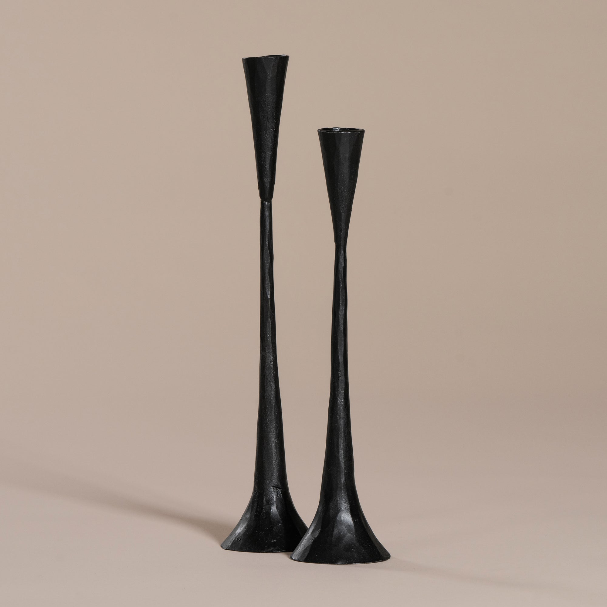 A set of two black metal taper candle holders with a modern sculptural design, featuring a handcrafted, elongated silhouette against a neutral background