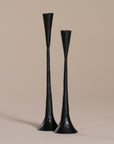 A set of two black metal taper candle holders with a modern sculptural design, featuring a handcrafted, elongated silhouette against a neutral background