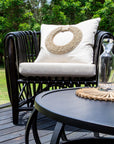 Black rattan lounge chair with neutral cushion and decorative shell pillow, styled on an outdoor deck with a black round coffee table and glassware