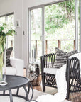 Modern living room featuring a black rattan lounge chair with a neutral cushion, accented with monochrome decor and lush greenery views