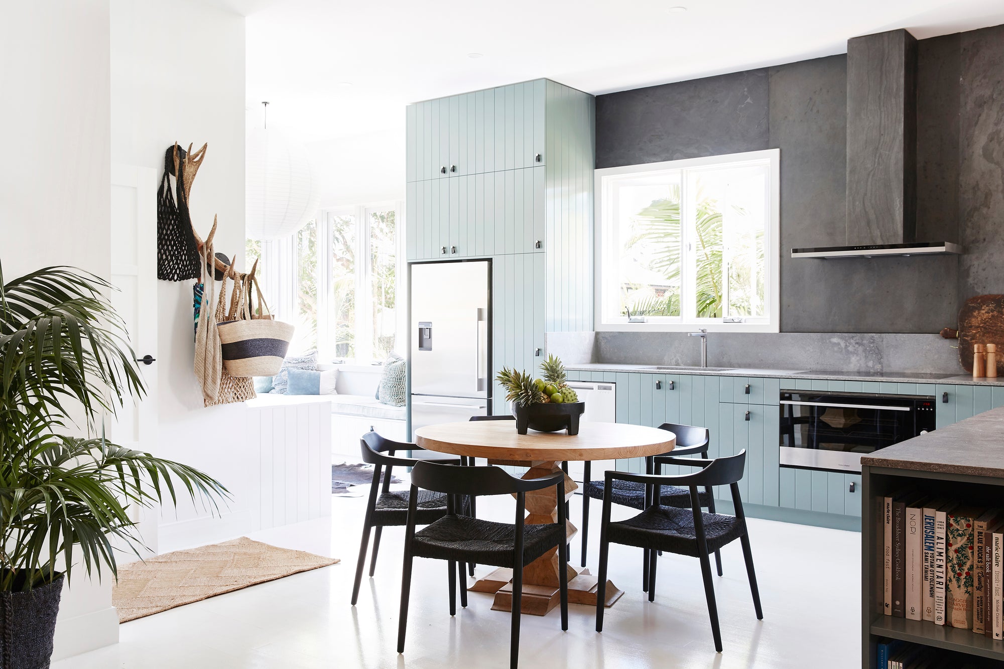 Contemporary kitchen with a round wooden dining table and black woven dining chairs. Featuring soft blue cabinetry, sleek black accents, and a light-filled interior for a modern coastal aesthetic