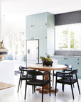 Contemporary kitchen with a round wooden dining table and black woven dining chairs. Featuring soft blue cabinetry, sleek black accents, and a light-filled interior for a modern coastal aesthetic