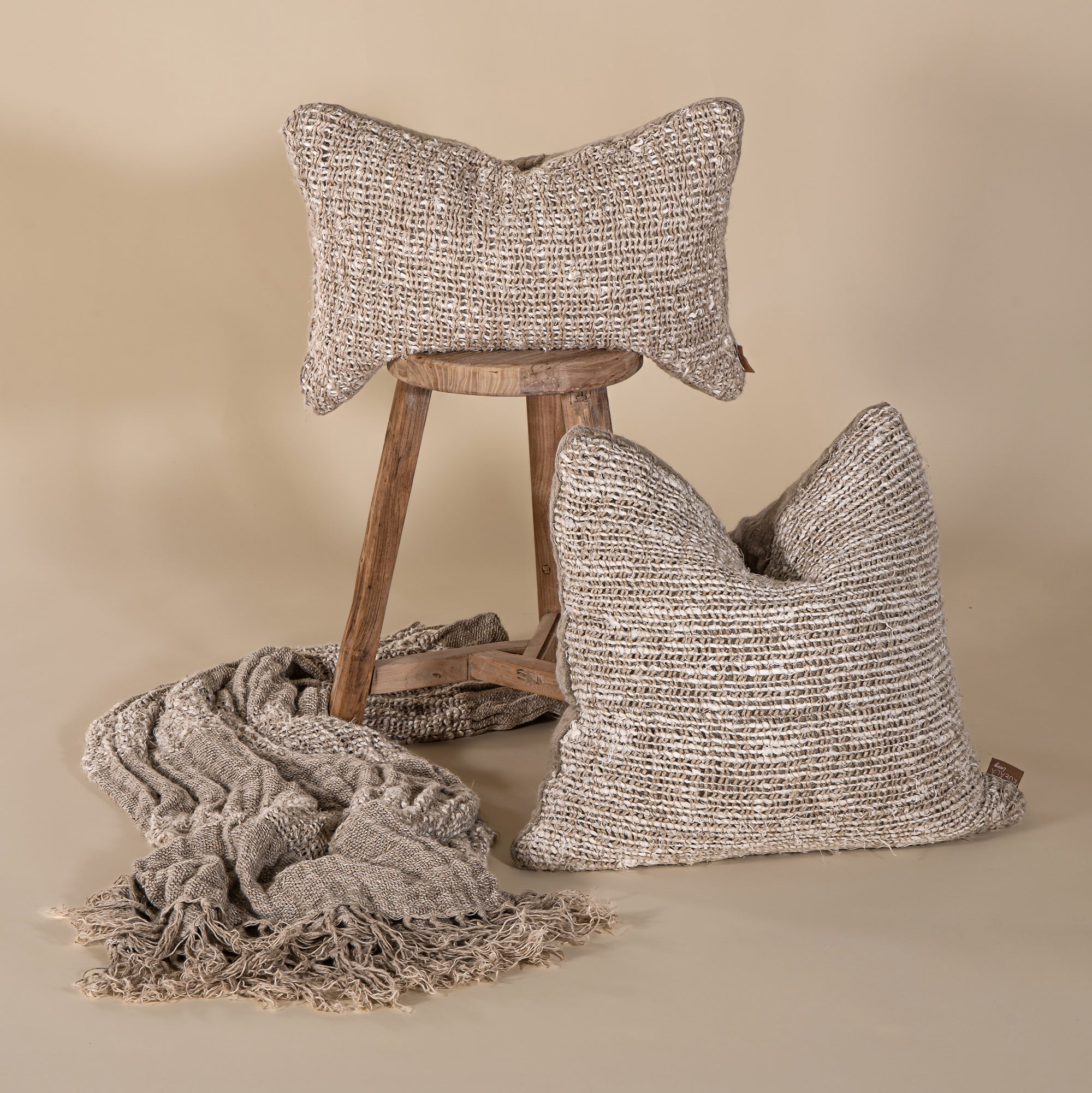 Handwoven natural cushions and throw styled with a rustic wooden stool, showcasing soft textures in warm neutral tones