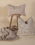 Handwoven natural cushions and throw styled with a rustic wooden stool, showcasing soft textures in warm neutral tones