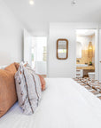 Modern coastal bedroom with neutral-toned bedding, textured cushions, and an ensuite featuring a rattan pendant light and earthy finishes