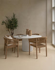 Modern dining space featuring a white fluted round dining table surrounded by woven armchairs in natural timber. Styled with wooden vases, ceramic tableware, and an olive tree, creating a warm, neutral-toned aesthetic.