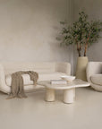 A modern, minimalist lounge setting featuring the KULALA Living curved bouclé sofa and matching armchair in a soft ivory hue. Styled with a textured throw, linen cushions, a sculptural stone coffee table, and a statement vase with an olive tree for a tranquil, contemporary aesthetic