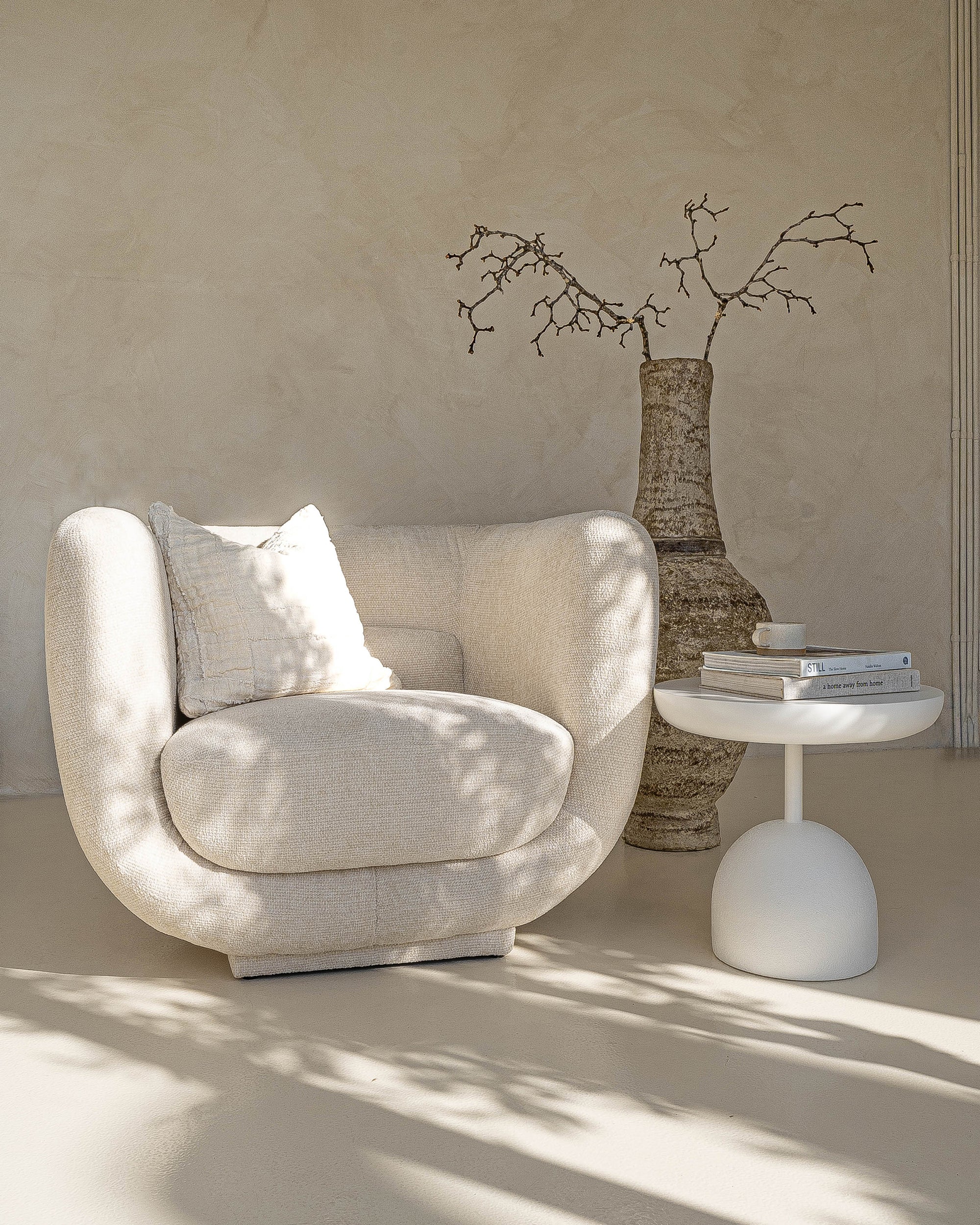 A serene living space featuring the KULALA Living curved bouclé chair in a soft ivory tone. Styled with a textured cushion, sculptural side table, and an earthy vase for a relaxed, modern aesthetic