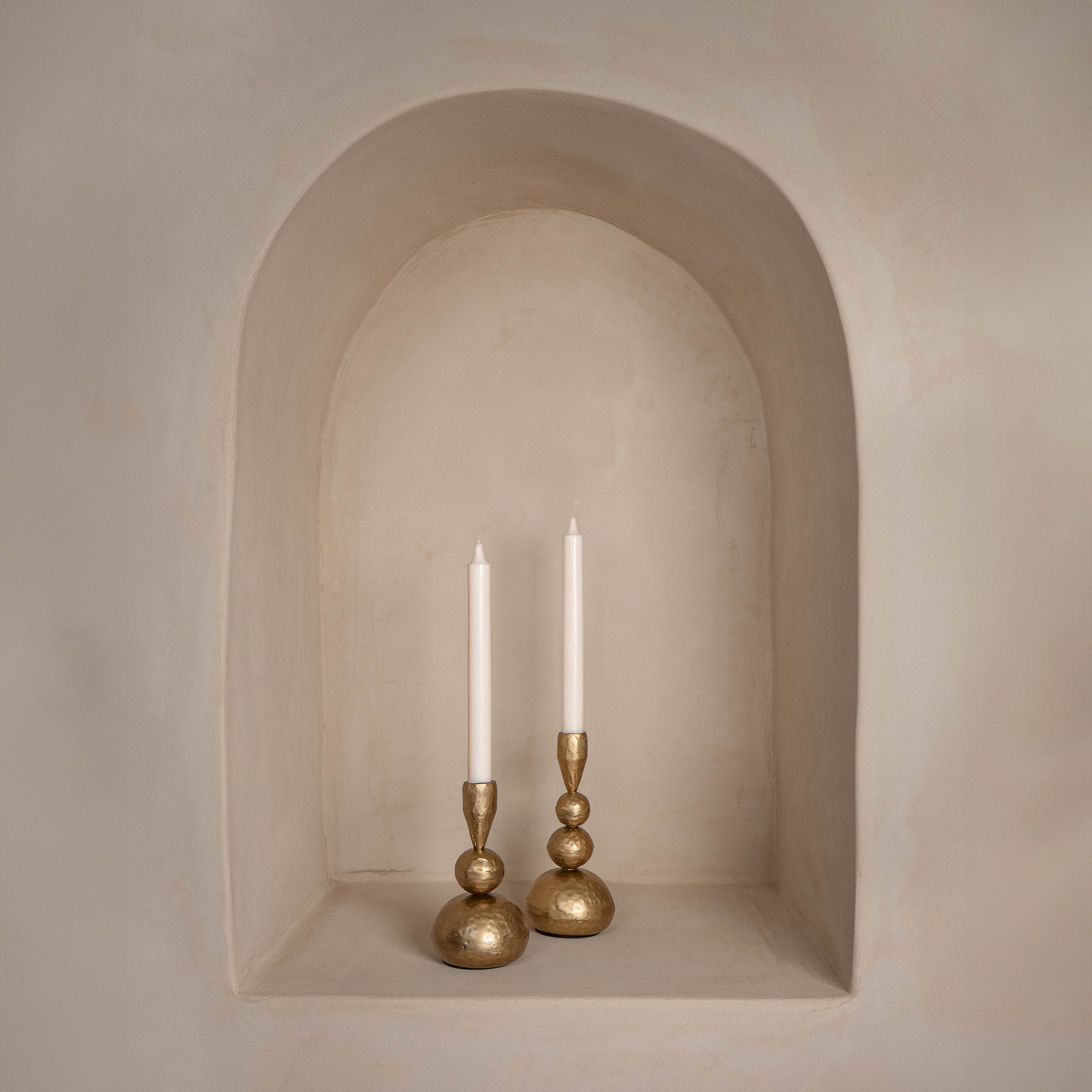 A pair of gold sculptural candlesticks with a polished brass finish styled in an arched wall niche