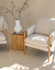 A beautifully styled pair of Hamptons-inspired armchairs from KULALA Living, featuring natural oak frames and soft linen upholstery. Set in a serene, light-filled space with a rustic wooden side table and a ceramic vase, exuding relaxed elegance