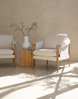 A beautifully styled pair of Hamptons-inspired armchairs from KULALA Living, featuring natural oak frames and soft linen upholstery. Set in a serene, light-filled space with a rustic wooden side table and a ceramic vase, exuding relaxed elegance