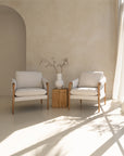 A beautifully styled pair of Hamptons-inspired armchairs from KULALA Living, featuring natural oak frames and soft linen upholstery. Set in a serene, light-filled space with a rustic wooden side table and a ceramic vase, exuding relaxed elegance