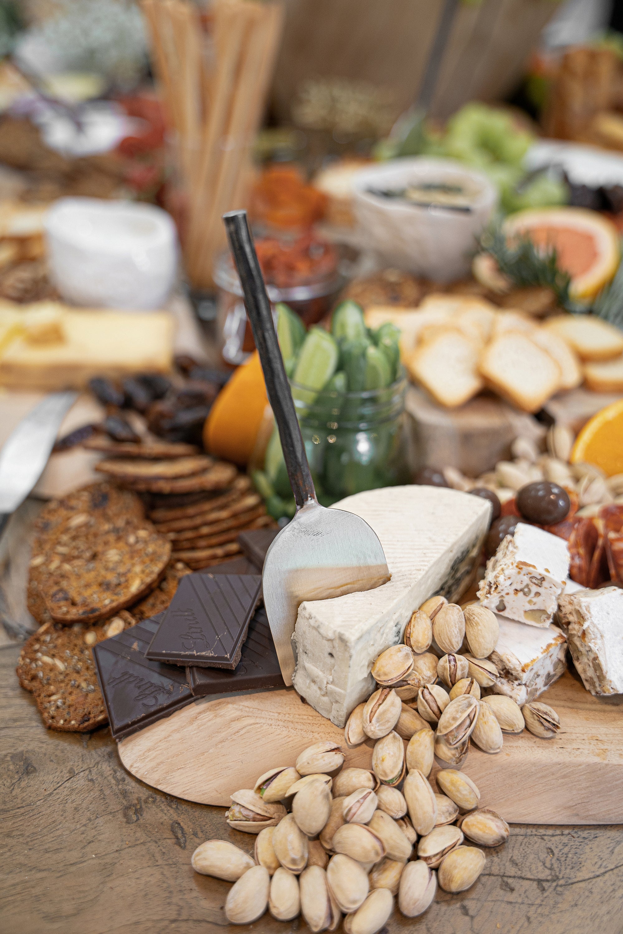 A beautifully styled grazing board featuring KULALA Living’s hand-forged cheese knife resting on a wedge of blue cheese, surrounded by gourmet crackers, dark chocolate, pistachios, and nougat. The perfect serving piece for effortless entertaining