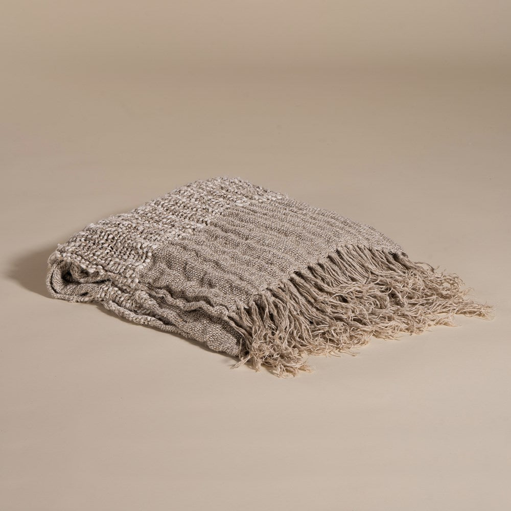 Handwoven fringed throw in a soft neutral tone, neatly folded to showcase its rich texture and intricate weave, perfect for layering in any living space