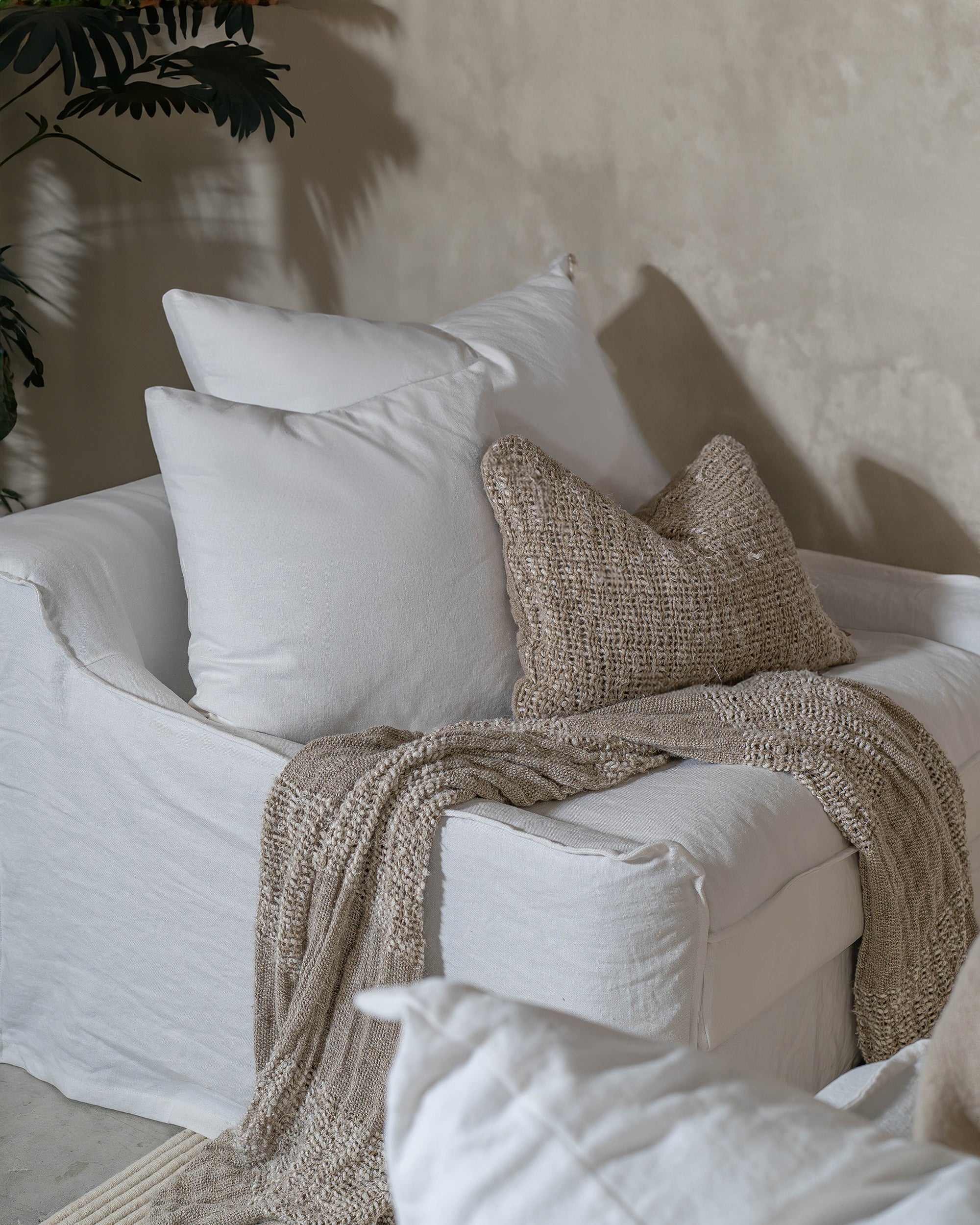 Handwoven natural throw draped over a white linen sofa, styled with textured neutral cushions to create a soft, inviting space