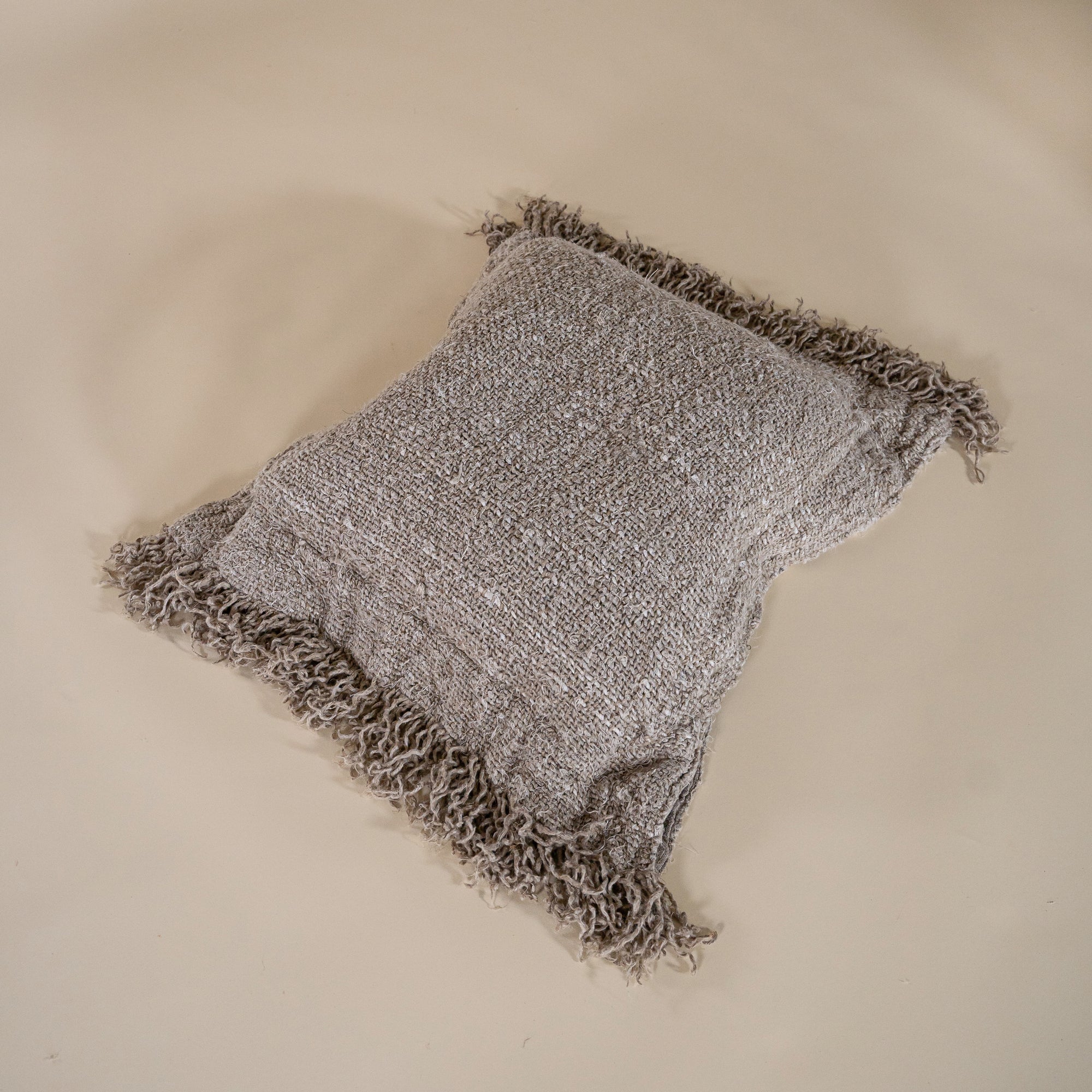 A handwoven cushion with natural fringe detailing, featuring an earthy, textured finish. This artisanal cushion adds warmth and organic style to any living space, complementing neutral and rustic interiors