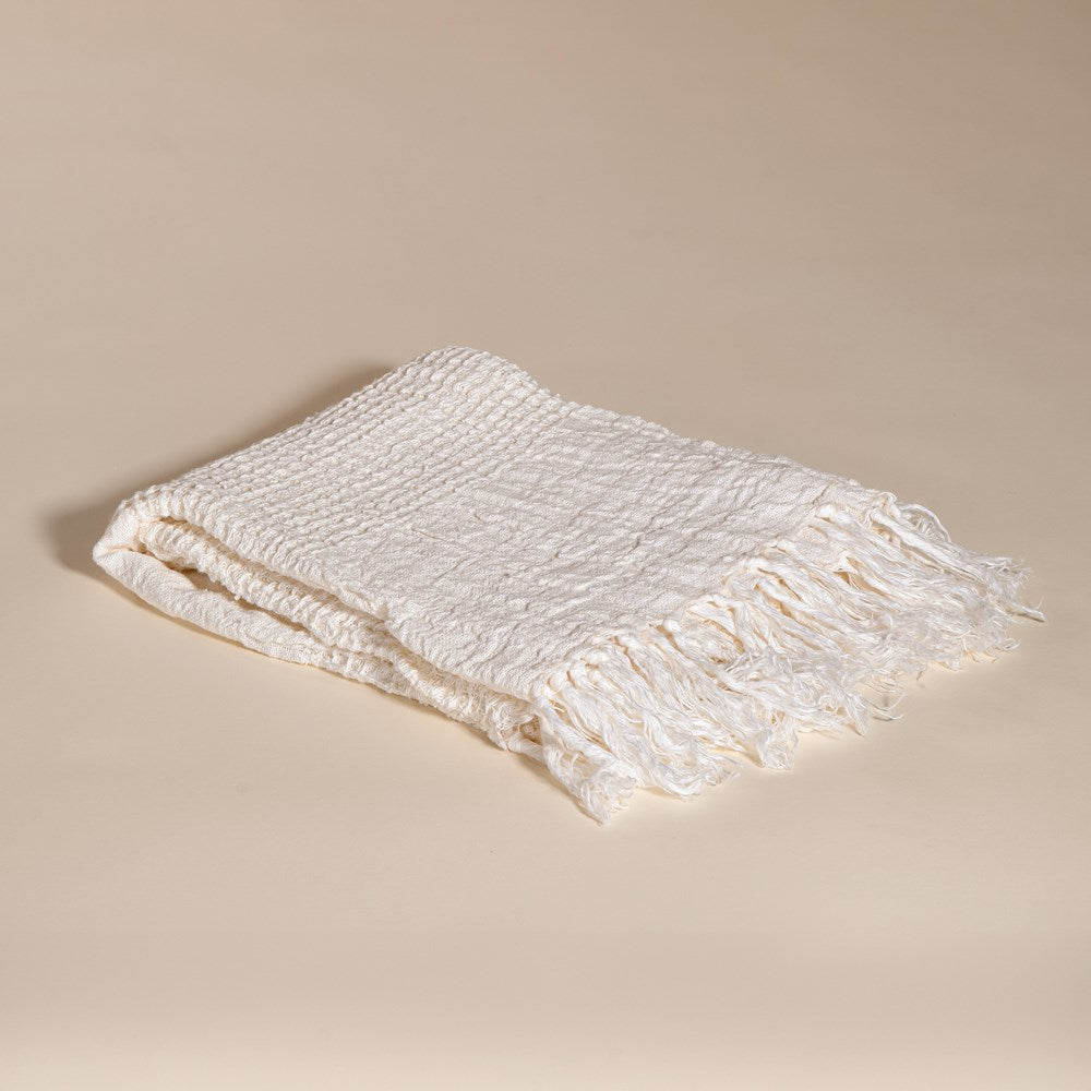 An elegant off-white handwoven linen throw from KULALA Living, featuring a soft texture and delicate fringed edges. A perfect layering piece for a relaxed, stylish home