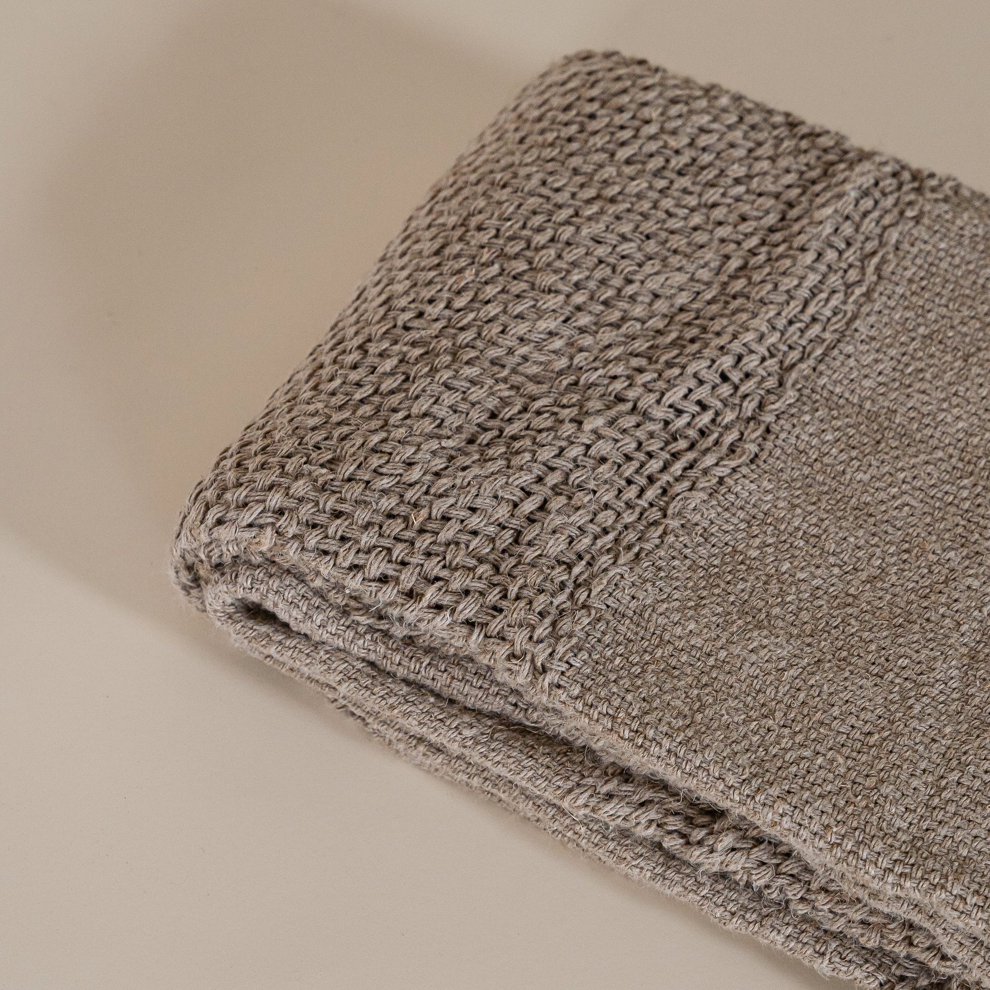 Handwoven natural fibre throw with intricate texture and fringed edges, folded elegantly against a neutral backdrop