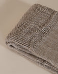 Handwoven natural fibre throw with intricate texture and fringed edges, folded elegantly against a neutral backdrop