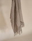 Handwoven natural fibre throw with intricate texture and fringed edges, draped elegantly against a neutral backdrop