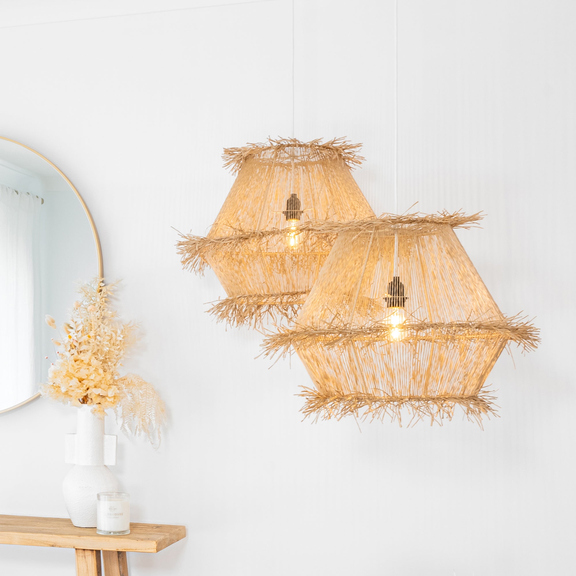 Pair of handwoven raffia pendant lights emitting a warm glow, styled in a minimalist interior with natural textures and soft lighting