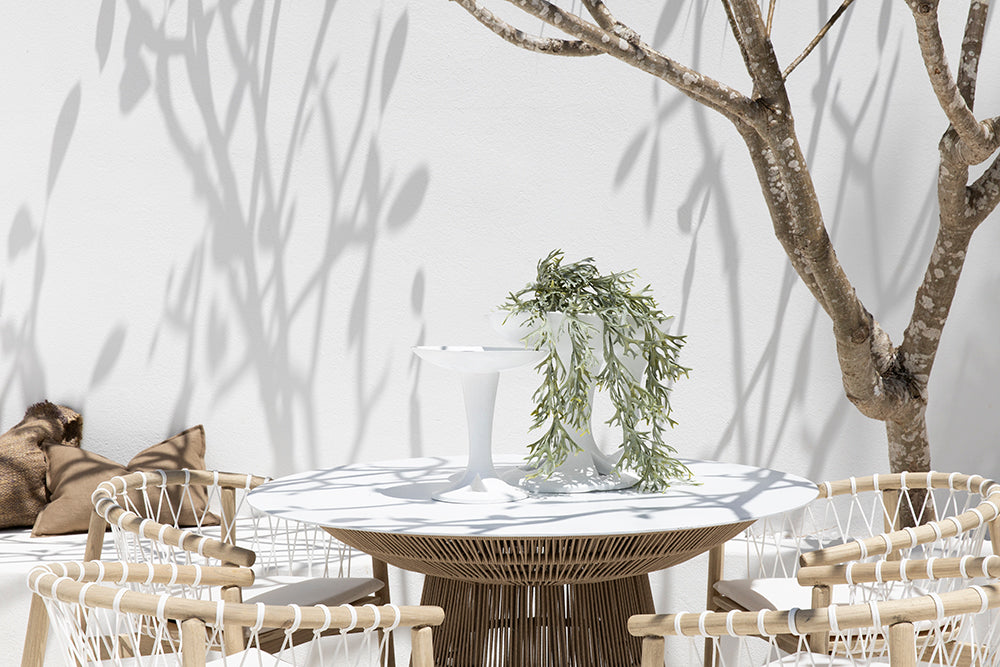 Spacious outdoor dining table with a woven rope base and white stone top, surrounded by natural wood chairs