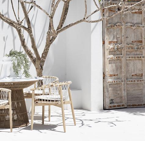 Spacious outdoor dining table with a woven rope base and white stone top, surrounded by natural wood chairs