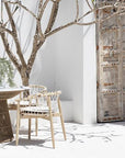 Spacious outdoor dining table with a woven rope base and white stone top, surrounded by natural wood chairs