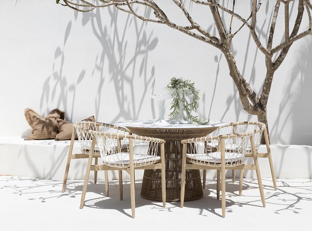 Spacious outdoor dining table with a woven rope base and white stone top, surrounded by natural wood chairs