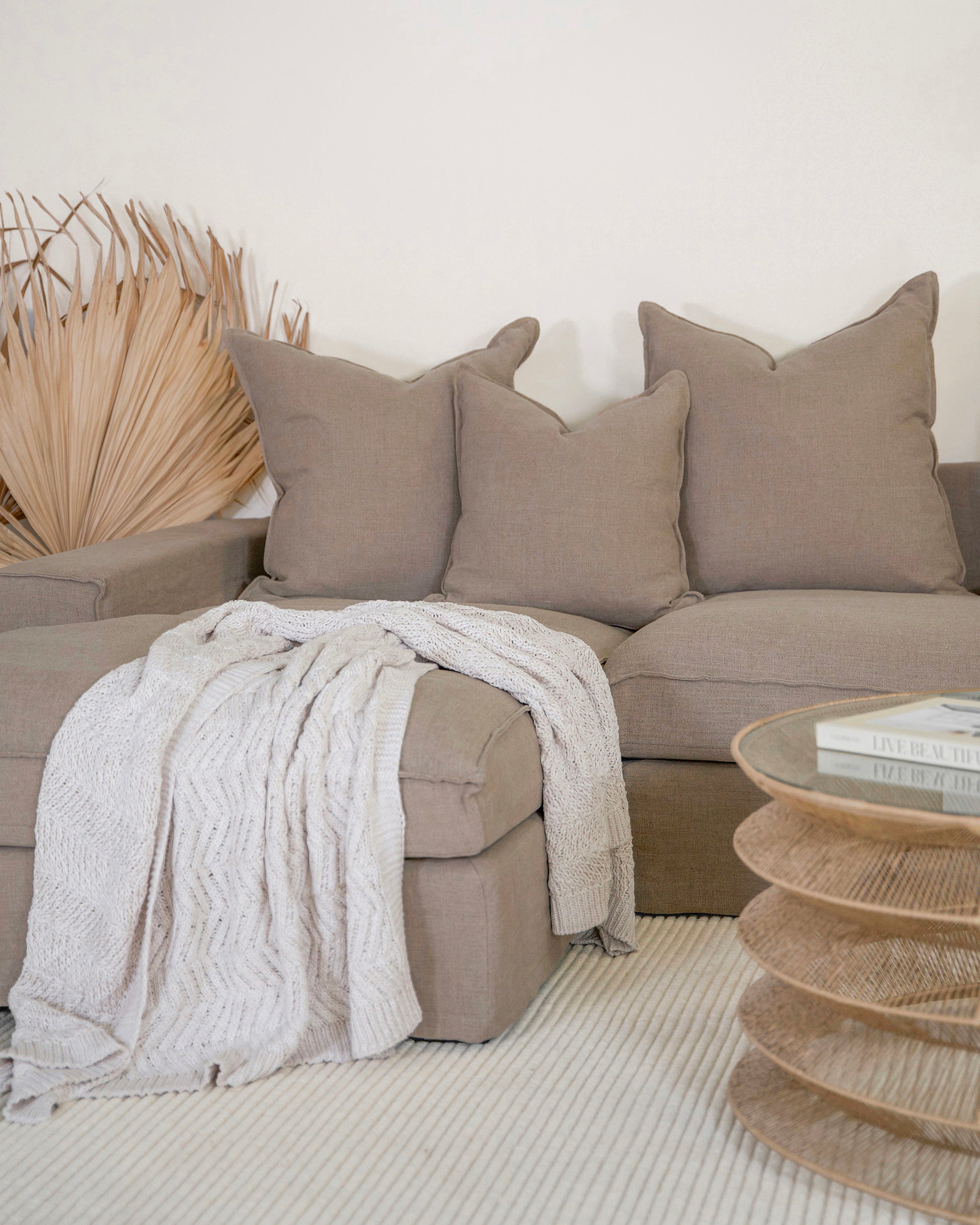 Linen slipcover sectional sofa styled in a modern living space. Showcasing plush neutral cushions, a textured throw, and a natural rattan coffee table for a relaxed, contemporary aesthetic.