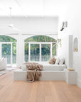 Serene minimalist bedroom featuring a white plaster bed, soft neutral-toned textiles, and large arched windows with lush green views, creating a tranquil retreat