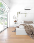 Minimalist bedroom with a white plaster bed, earthy-toned textured bedding, and soft natural light streaming through arched windows, creating a serene retreat